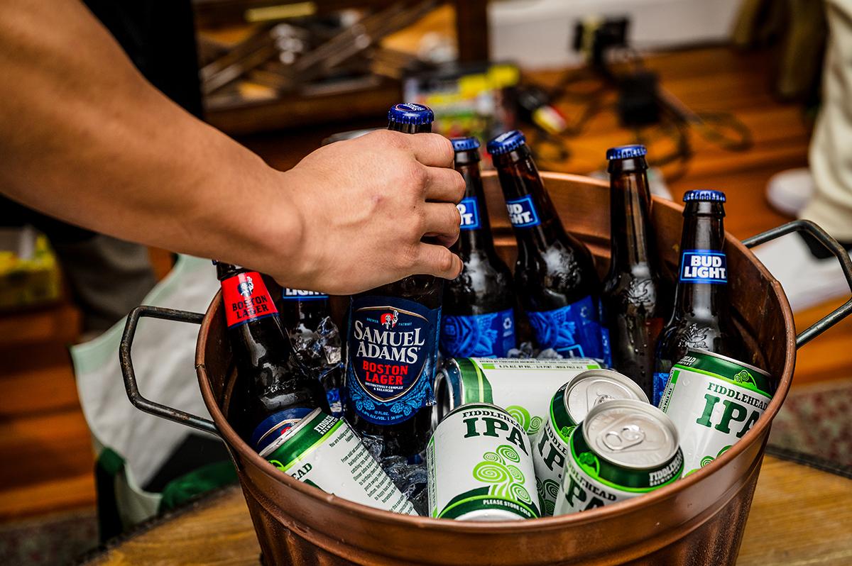 A hand grabs a beer bottle from a bucket filled with assorted beer bottles and cans.