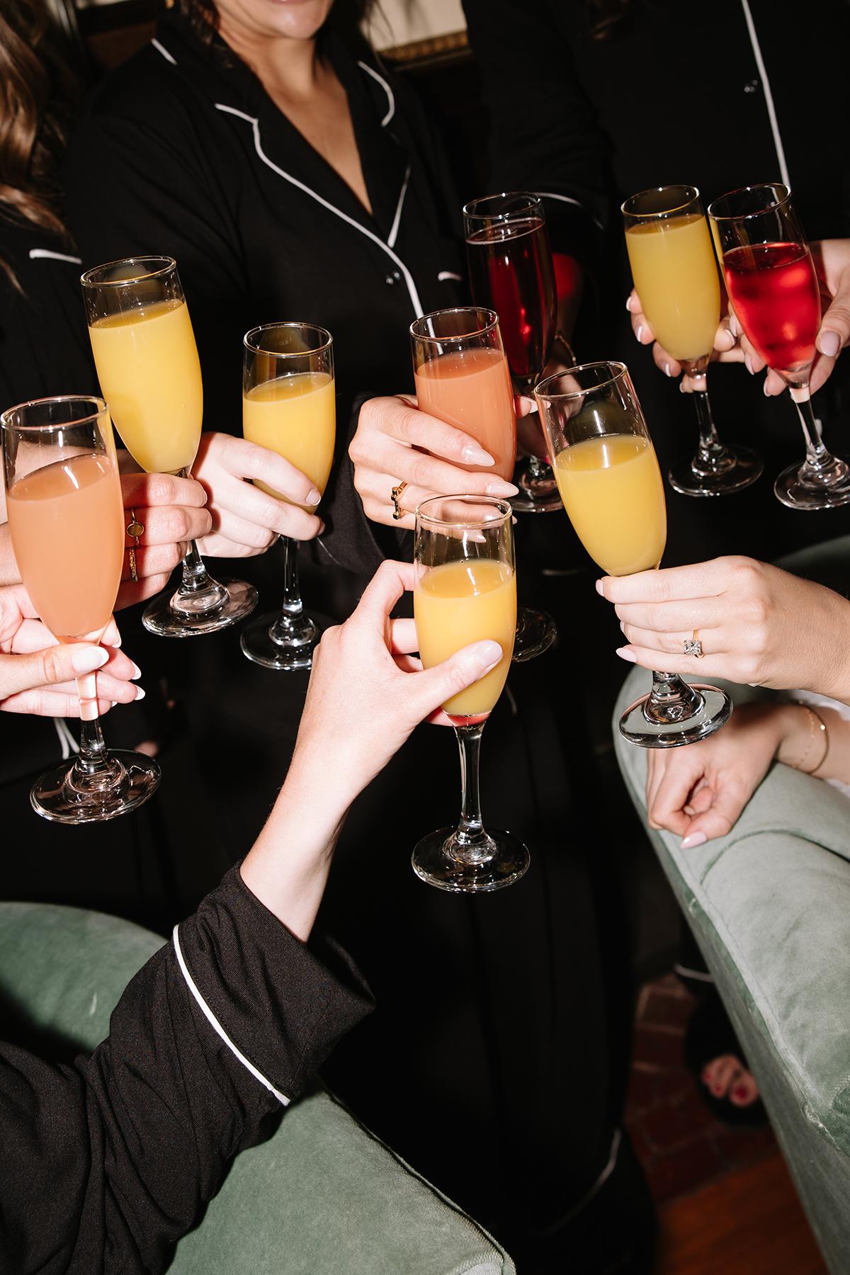 Cheers with colorful drinks in flutes, people in black outfits.