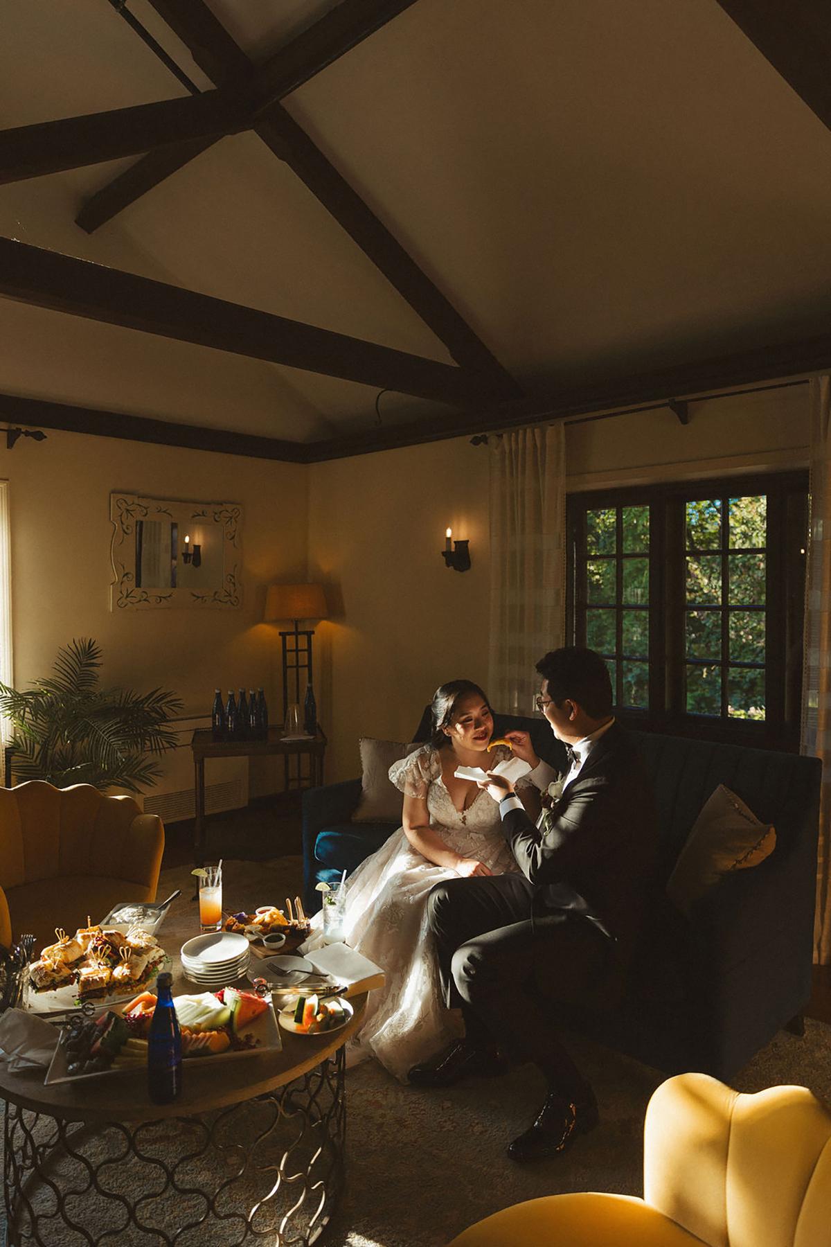 Couple in warm-lit room sharing a moment on a couch, surrounded by snacks.