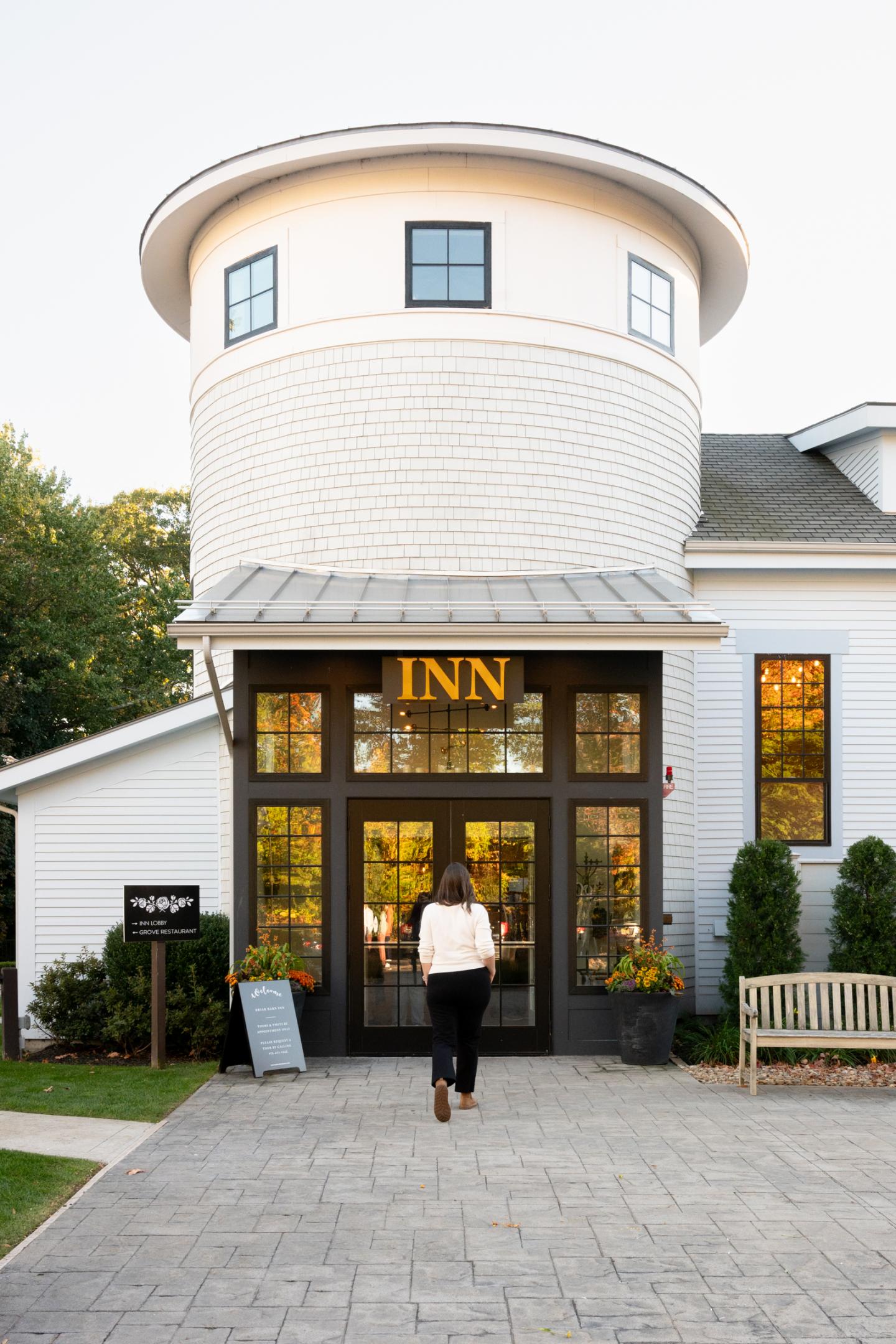 Woman entering a white inn with a round tower and large windows.