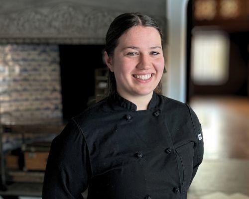 Chef in black uniform smiling in a warmly lit room.