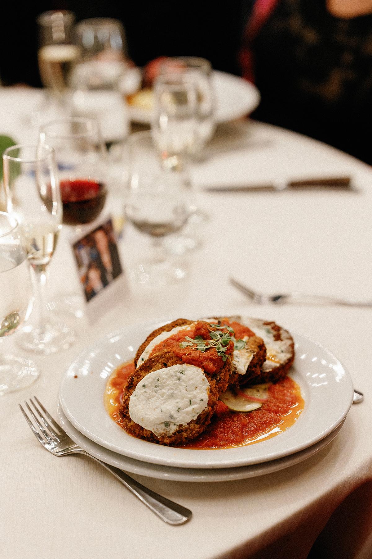 Eggplant Parmesan with tomato sauce on a white plate, set on a dining table.