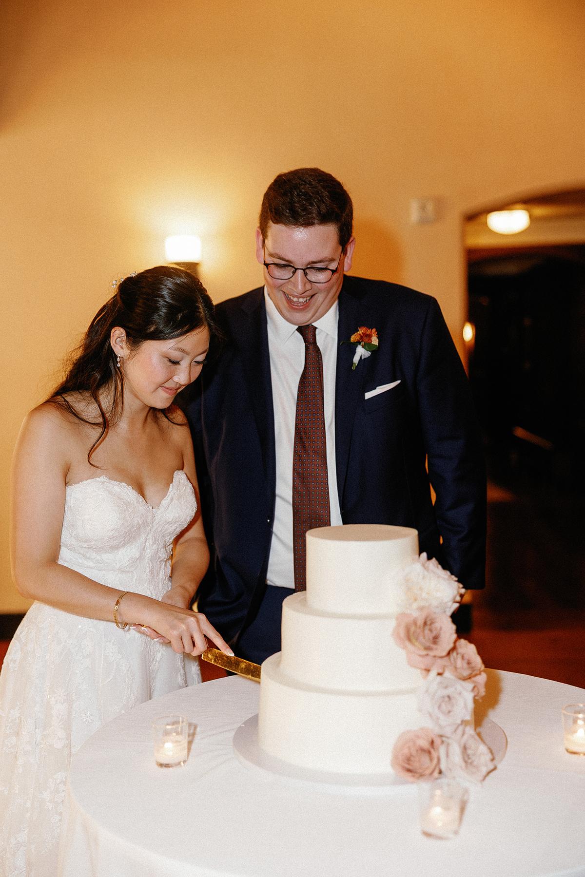 Couple cutting a three-tier wedding cake with flowers.