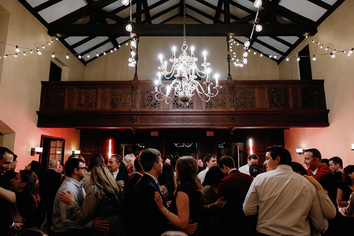 Guests dancing under chandeliers at a lively indoor event.