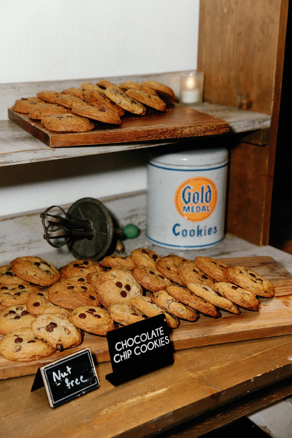 Chocolate chip cookies on wooden shelves beside a vintage cookie tin.