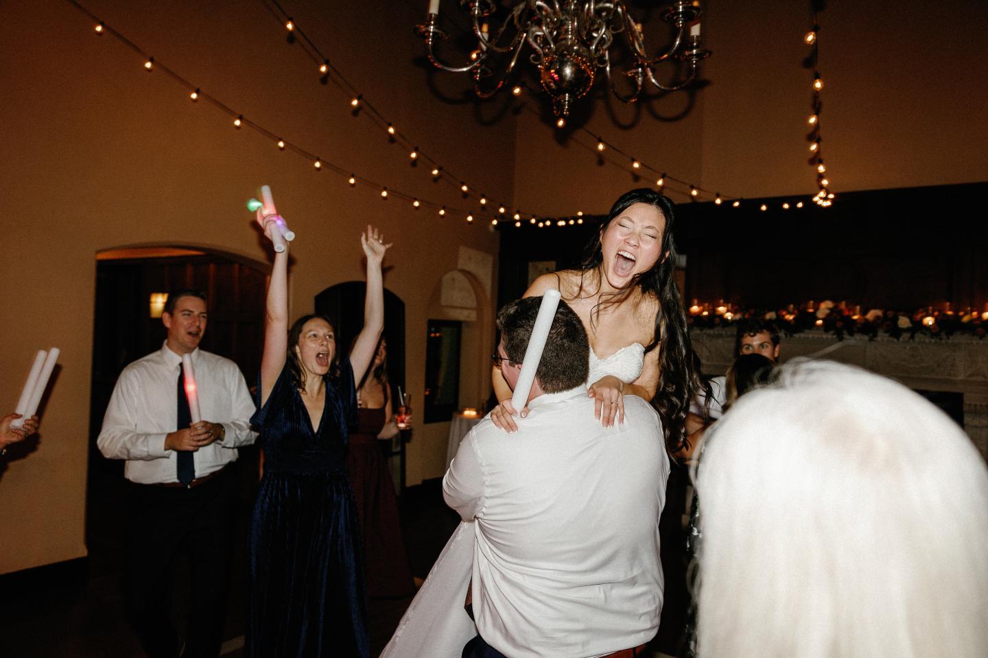 Joyful wedding celebration with dancing and laughter in a warmly lit room.