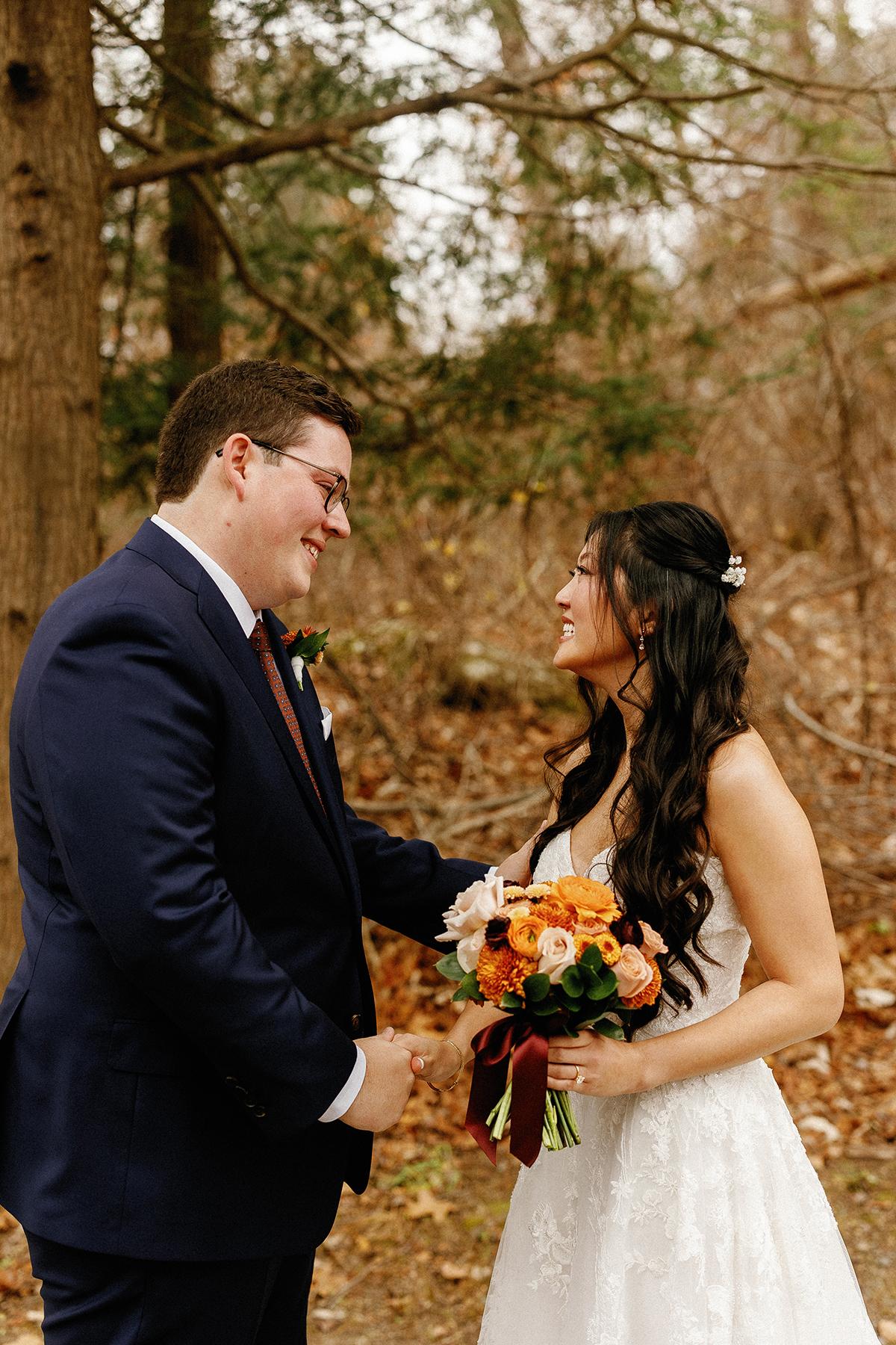 Couple in wedding attire smiling at each other in a forest setting.