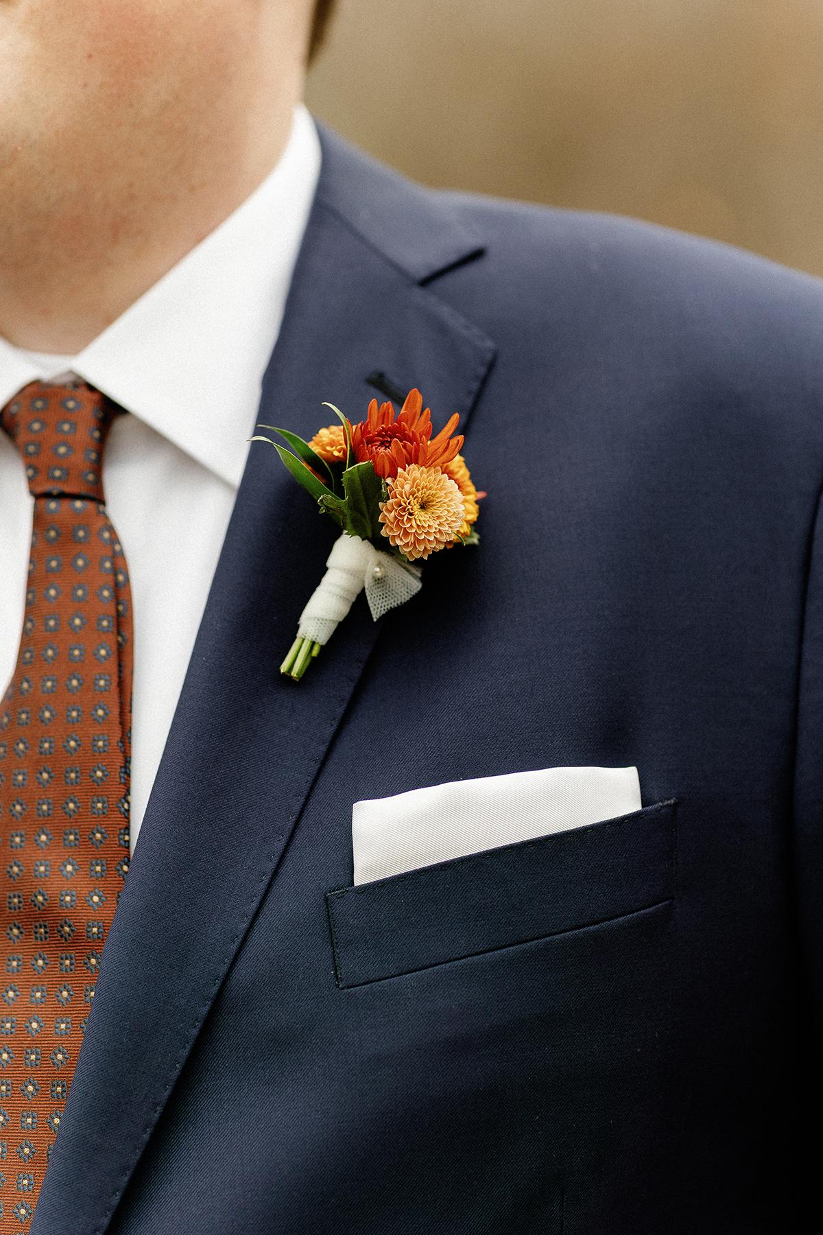 Navy suit, orange tie, flower boutonniere, white pocket square.