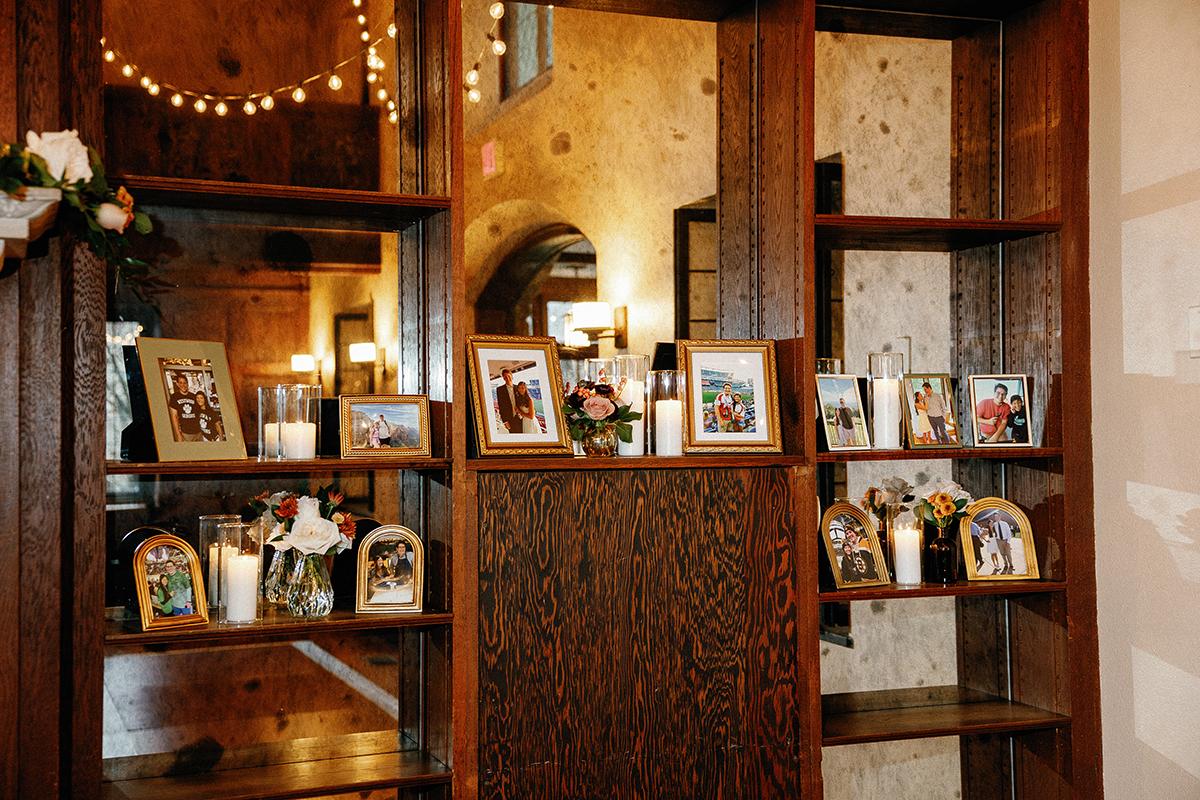 A shelf with framed family photos and candles in a warmly lit room.