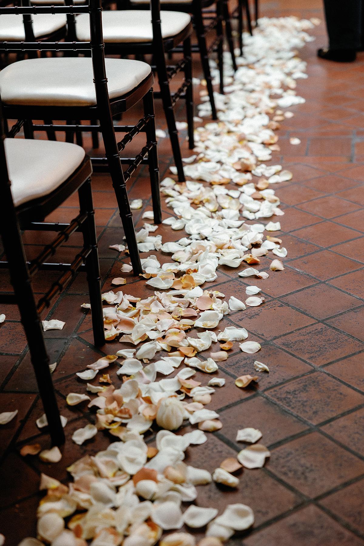 Rose petals scattered along a path between rows of chairs on a tiled floor.