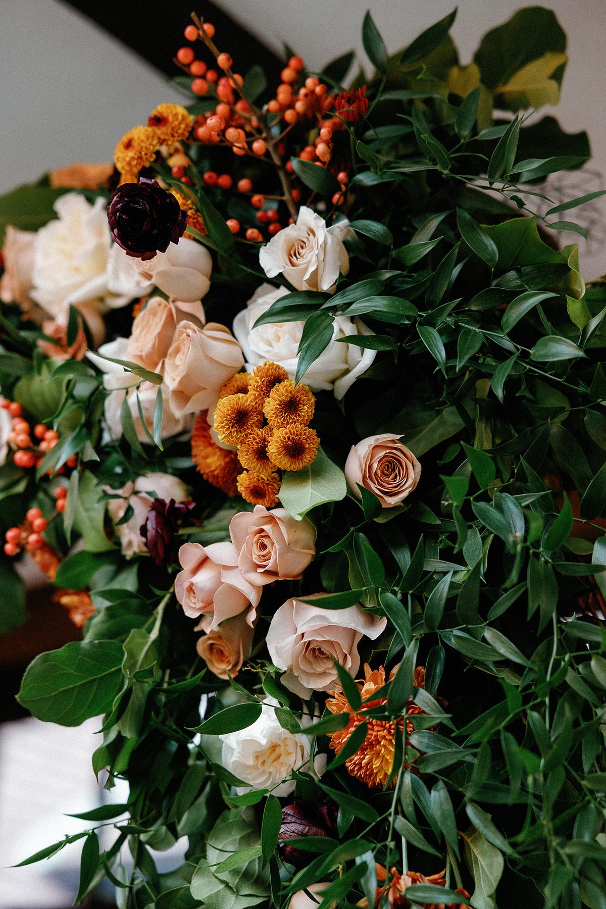 Colorful bouquet with roses, orange flowers, and green leaves.
