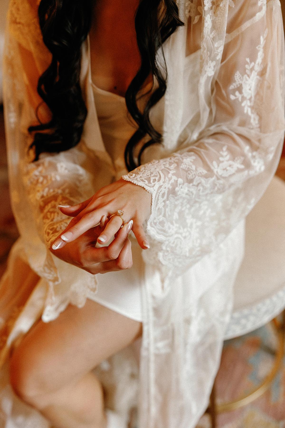Woman in lace robe sitting, hands clasped, with dark hair cascading over shoulders.