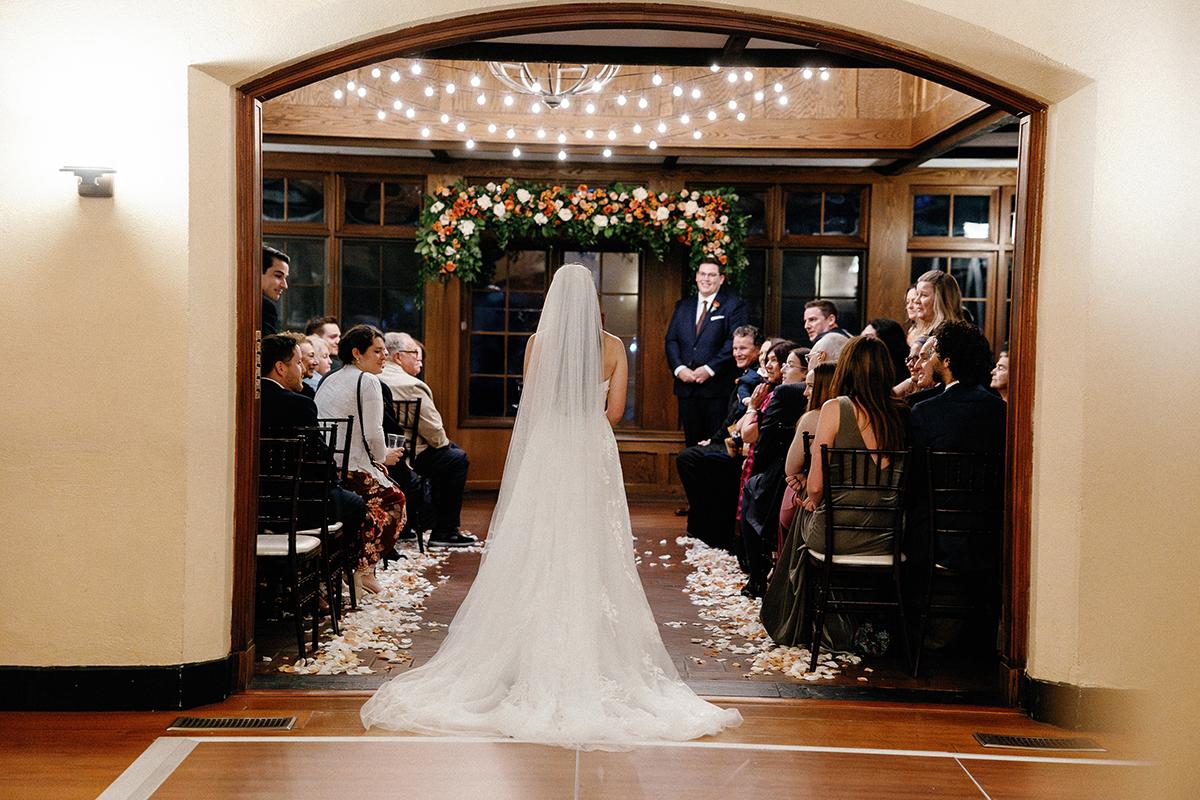 Bride walks down the aisle in a decorated indoor wedding ceremony.