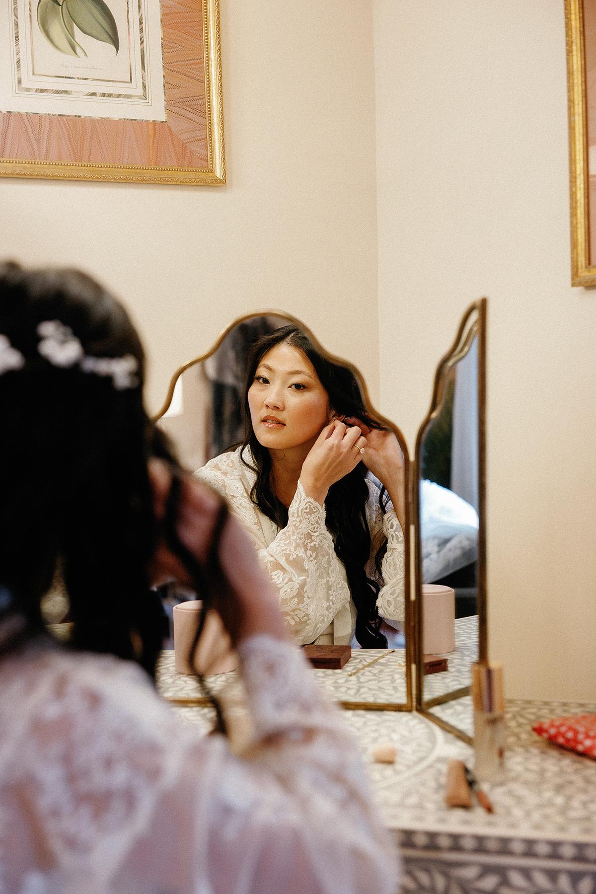 Woman in white lace adjusts hair in mirror reflection.
