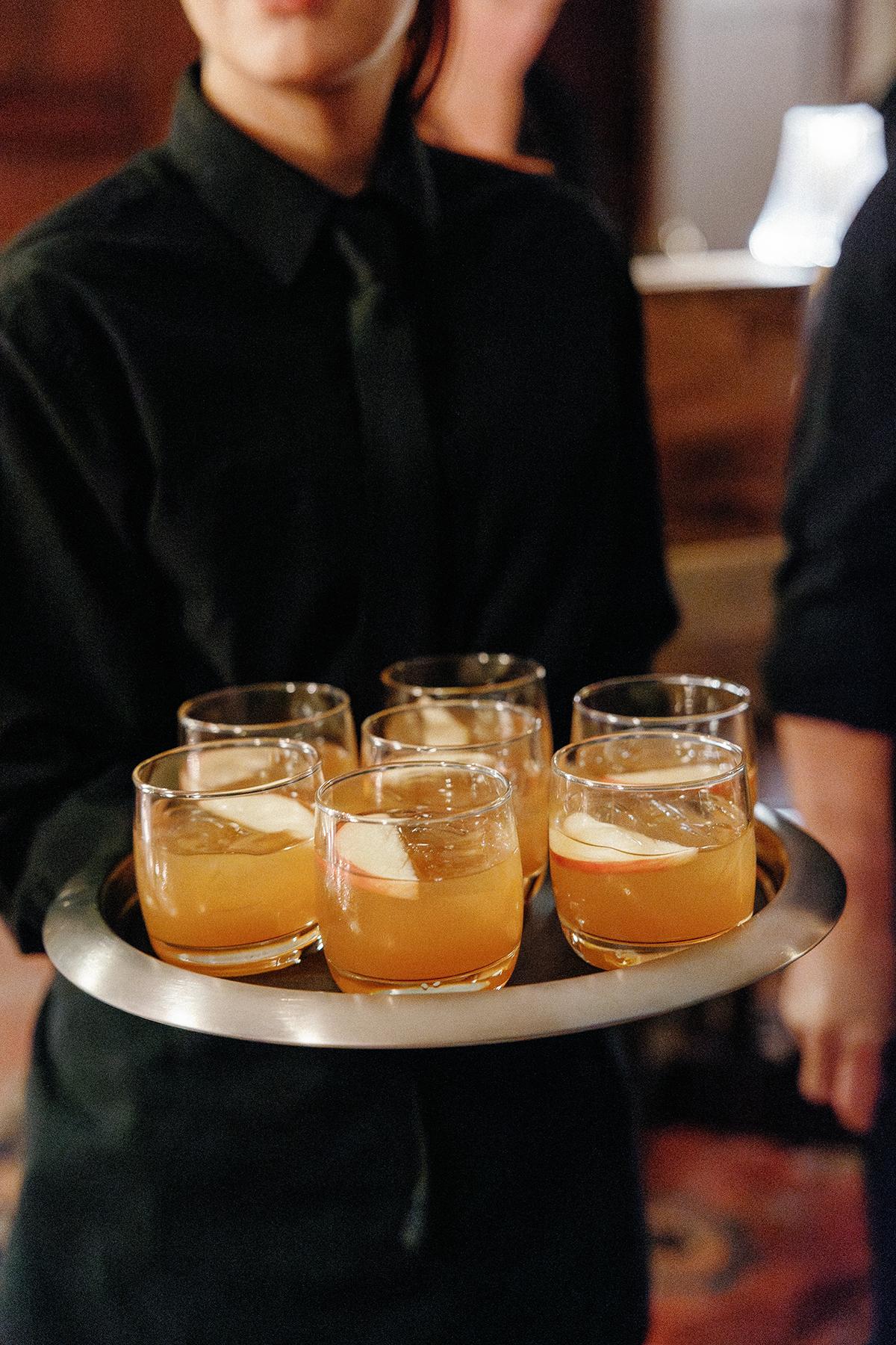 Server holding a tray of orange cocktails with ice.
