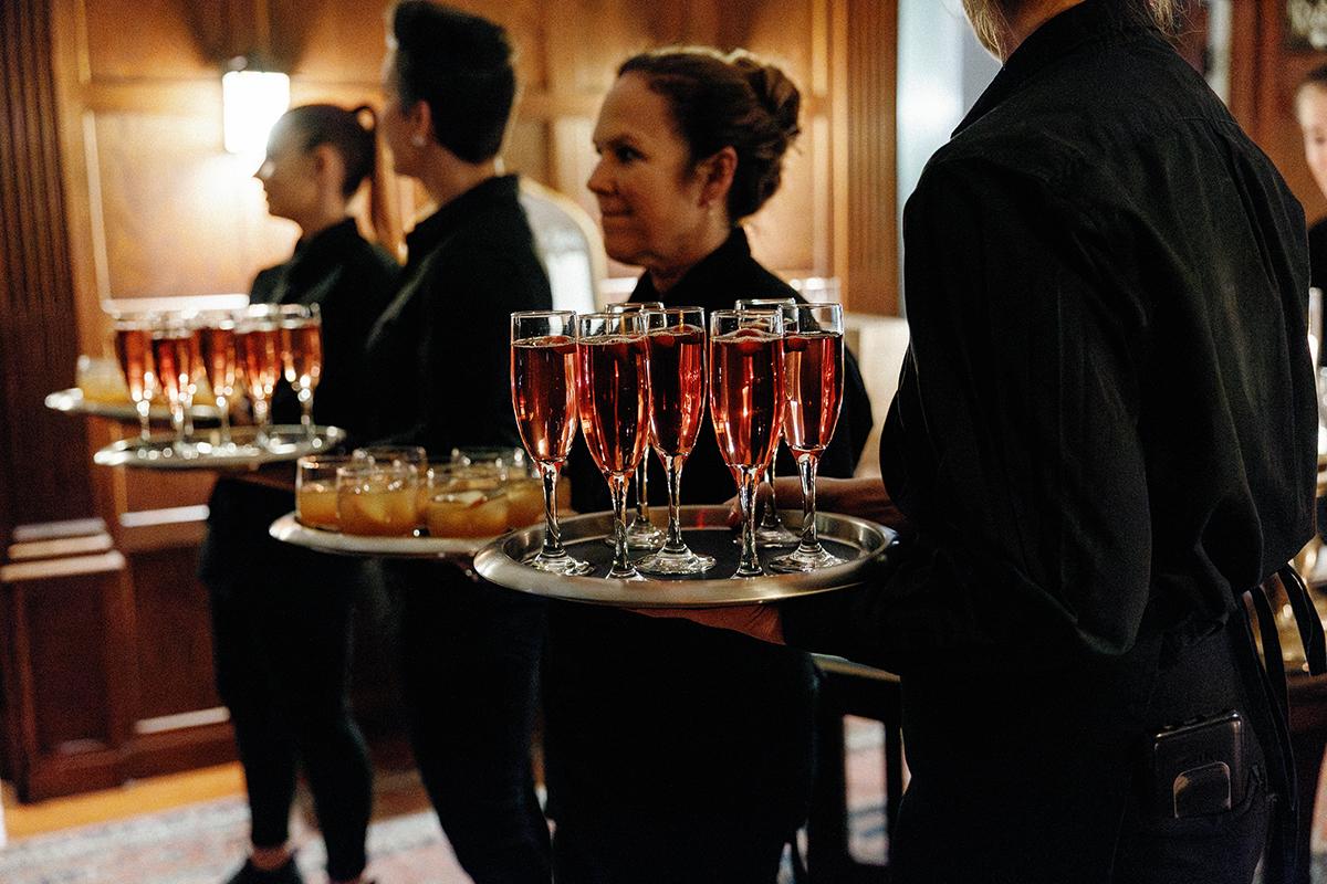Waitstaff holding trays of drinks in a dimly lit room.