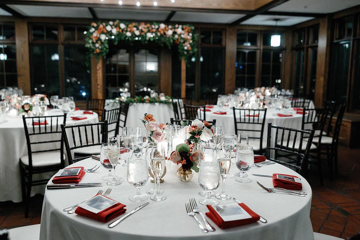 Elegant dining tables with white linens, red napkins, and floral centerpieces in a decorated hall.