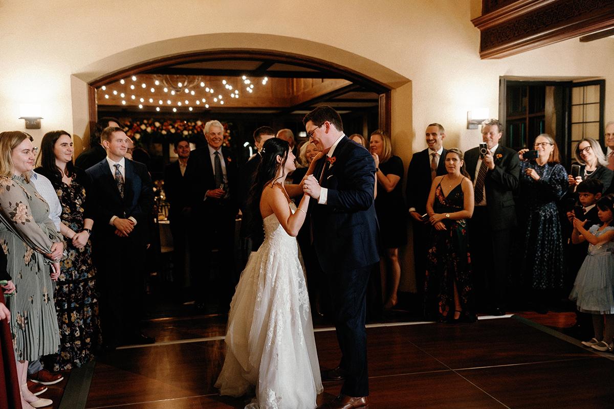 Bride and groom share first dance at a wedding reception, surrounded by guests.