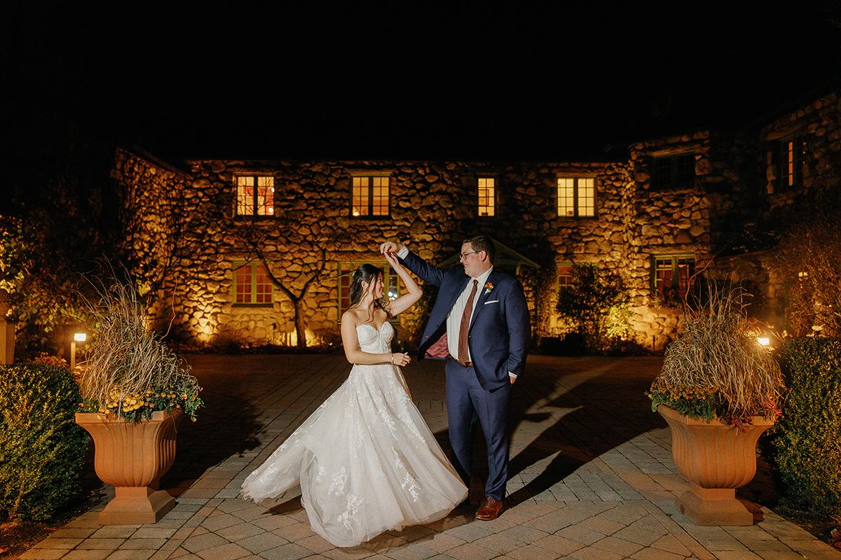 Bride and groom dancing outdoors at night, stone building in background.