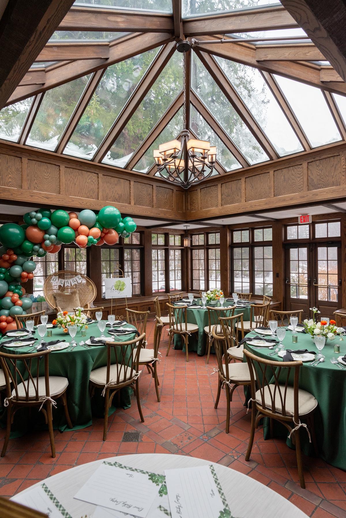 Decorated event room with green and copper balloons, round tables, and a skylight.