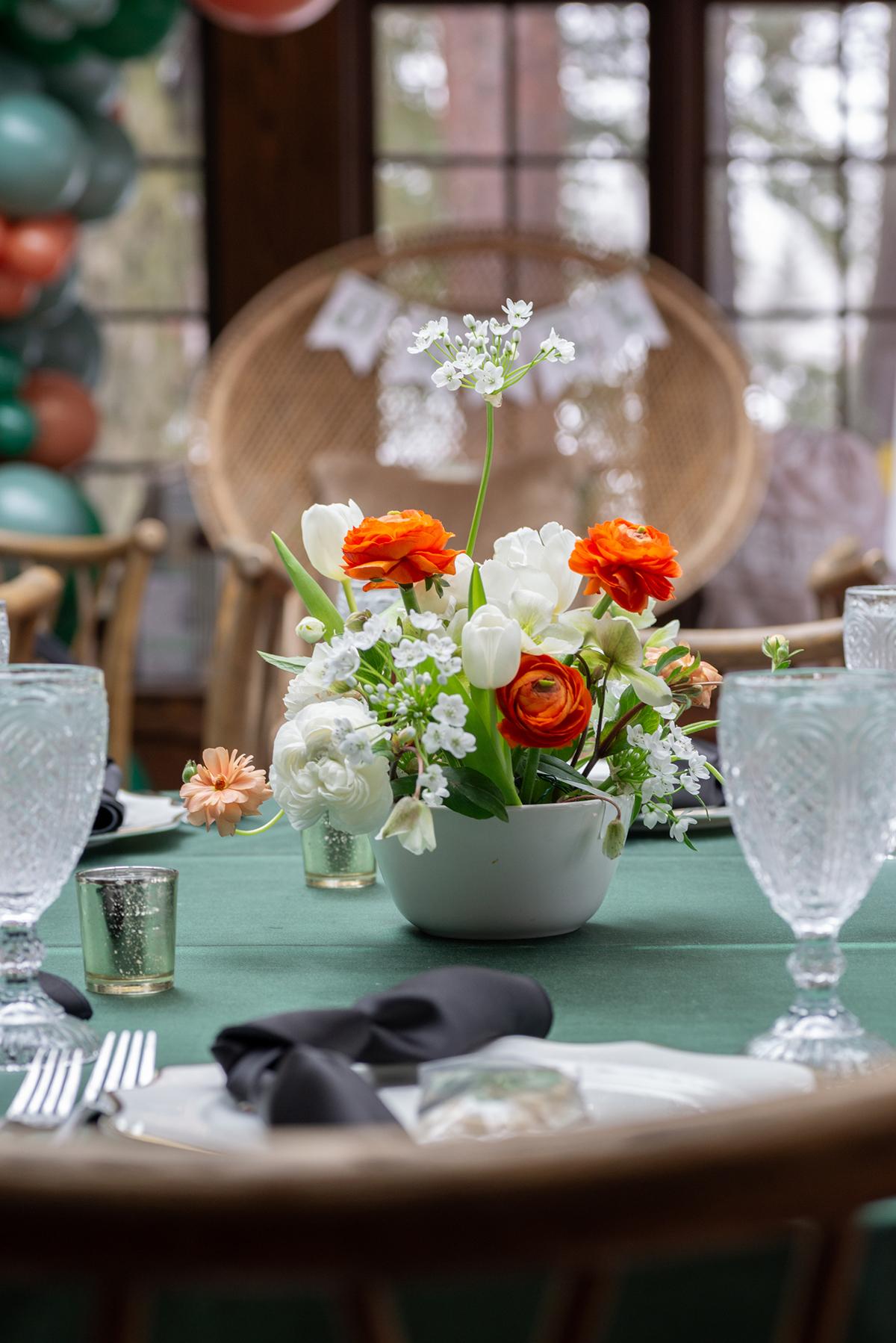 Flowers in a vase on a green tablecloth, with glasses and folded napkins nearby.