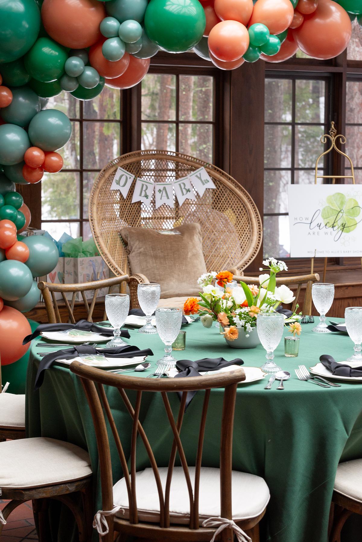 Dining table with green cloth, floral centerpiece, decorative balloons, and wicker chair.