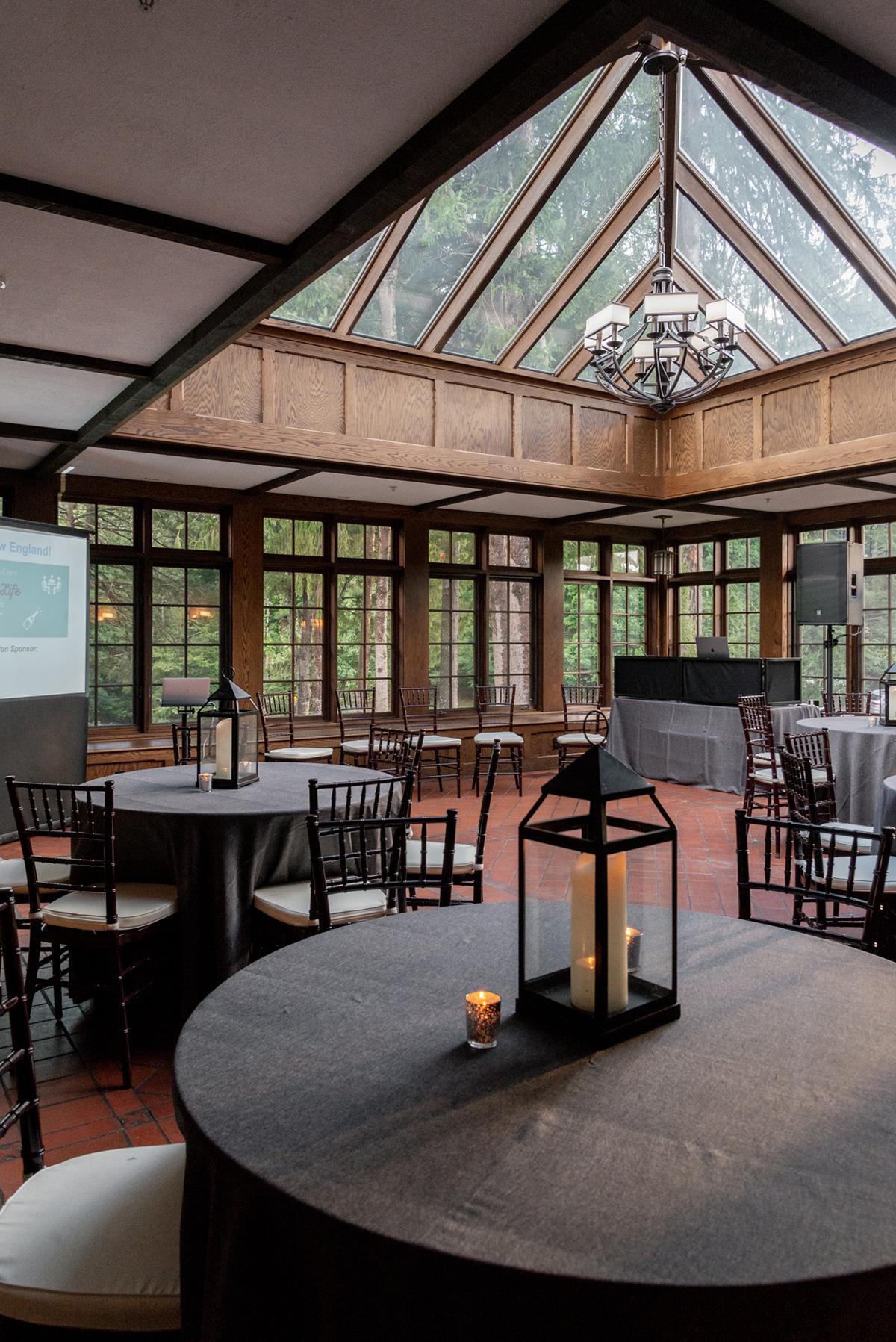 Elegant room with round tables, lanterns, and large windows under a glass ceiling.