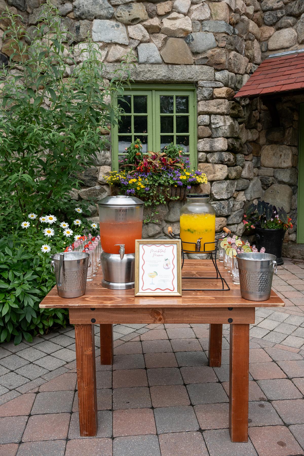 Table with lemonade and iced tea in front of stone cottage.