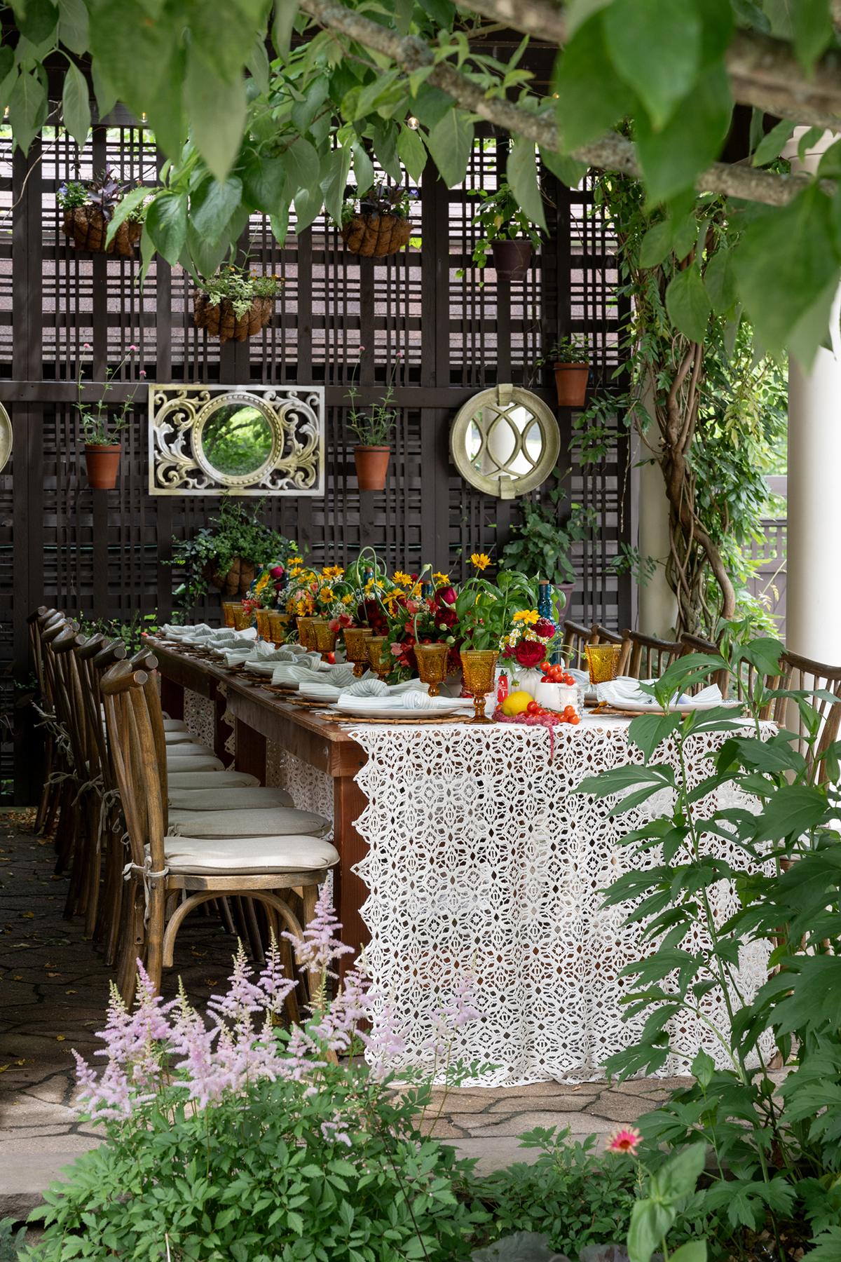 Long table set for a garden party, surrounded by greenery and flowers.