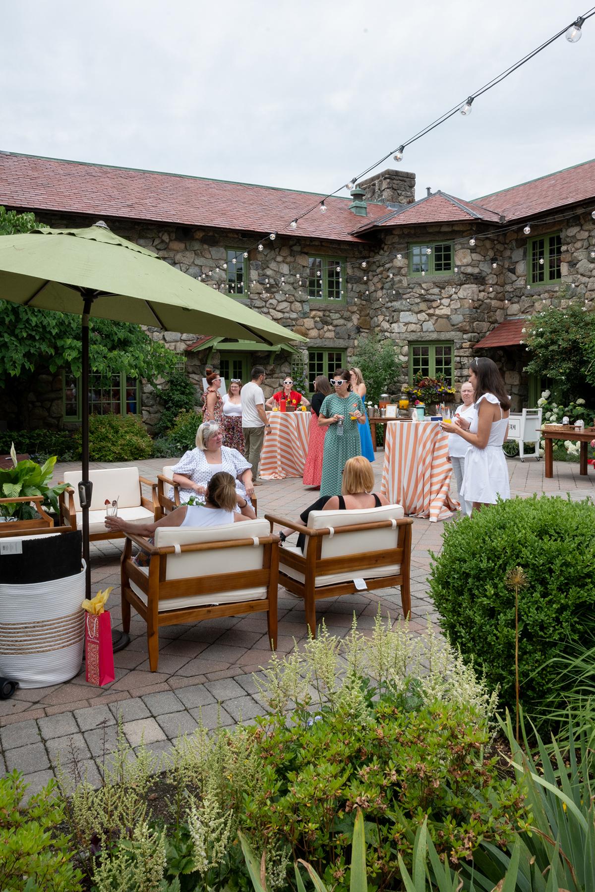 Outdoor gathering with people socializing under a green umbrella, near a stone building.