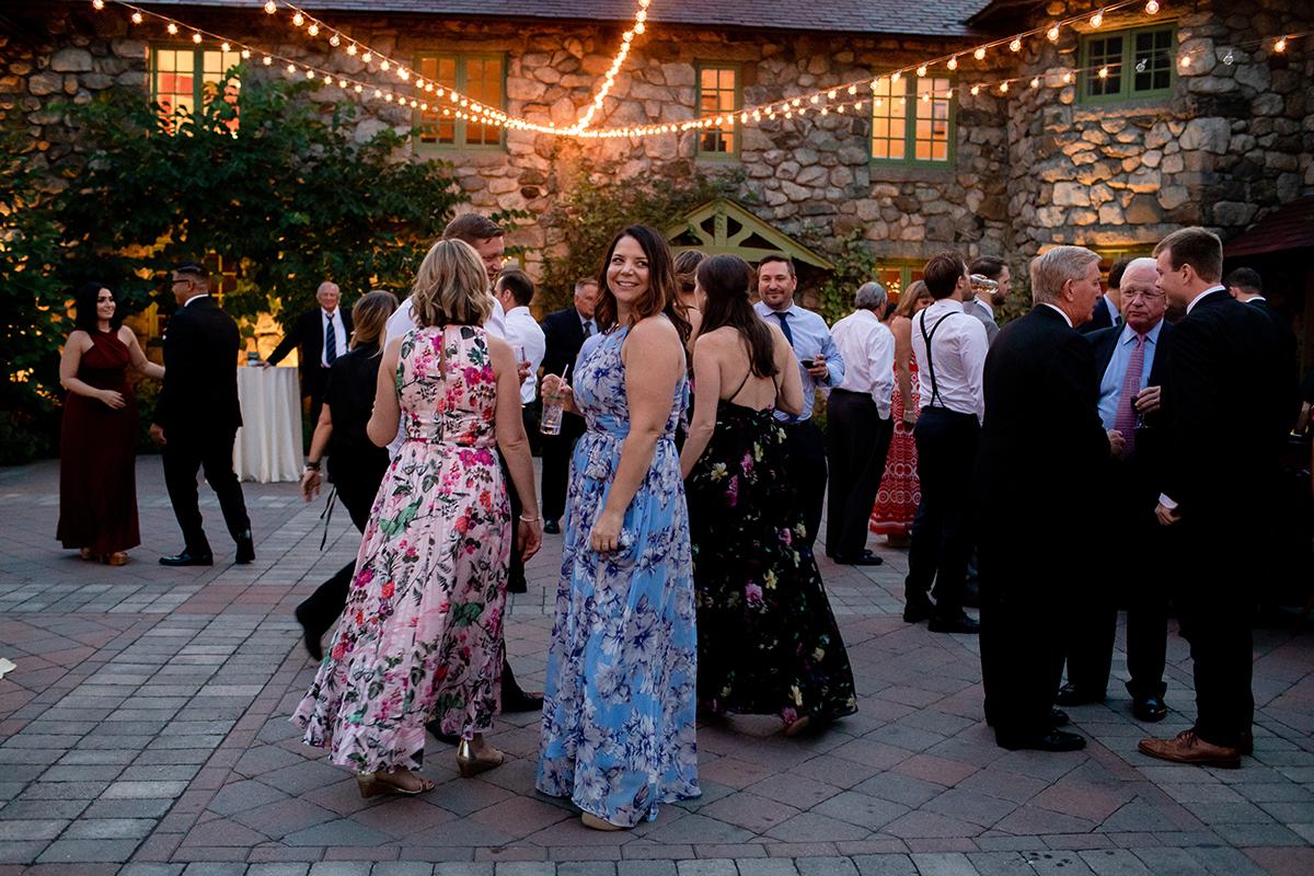 Outdoor wedding reception, guests in colorful dresses and suits, string lights overhead.