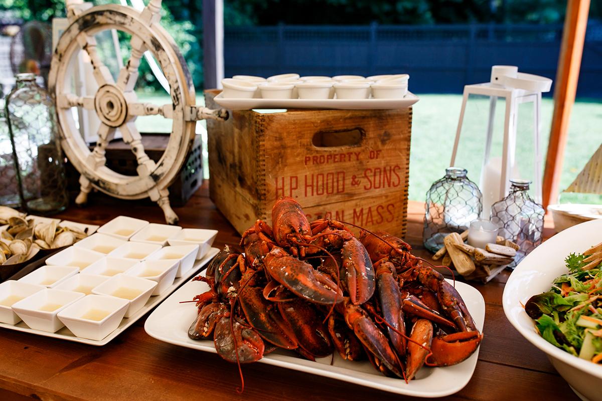 Rustic buffet with lobsters, salads, and nautical decor on a wooden table.