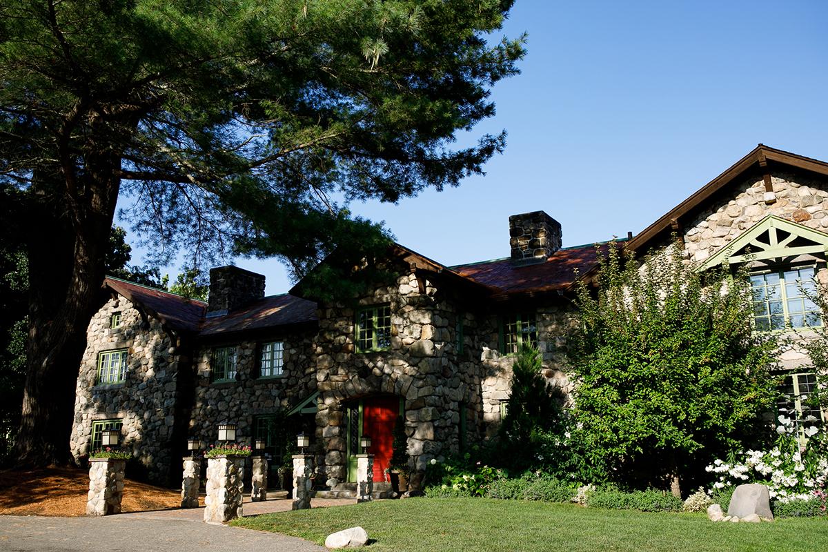 Stone house with red door surrounded by lush greenery and tall trees.