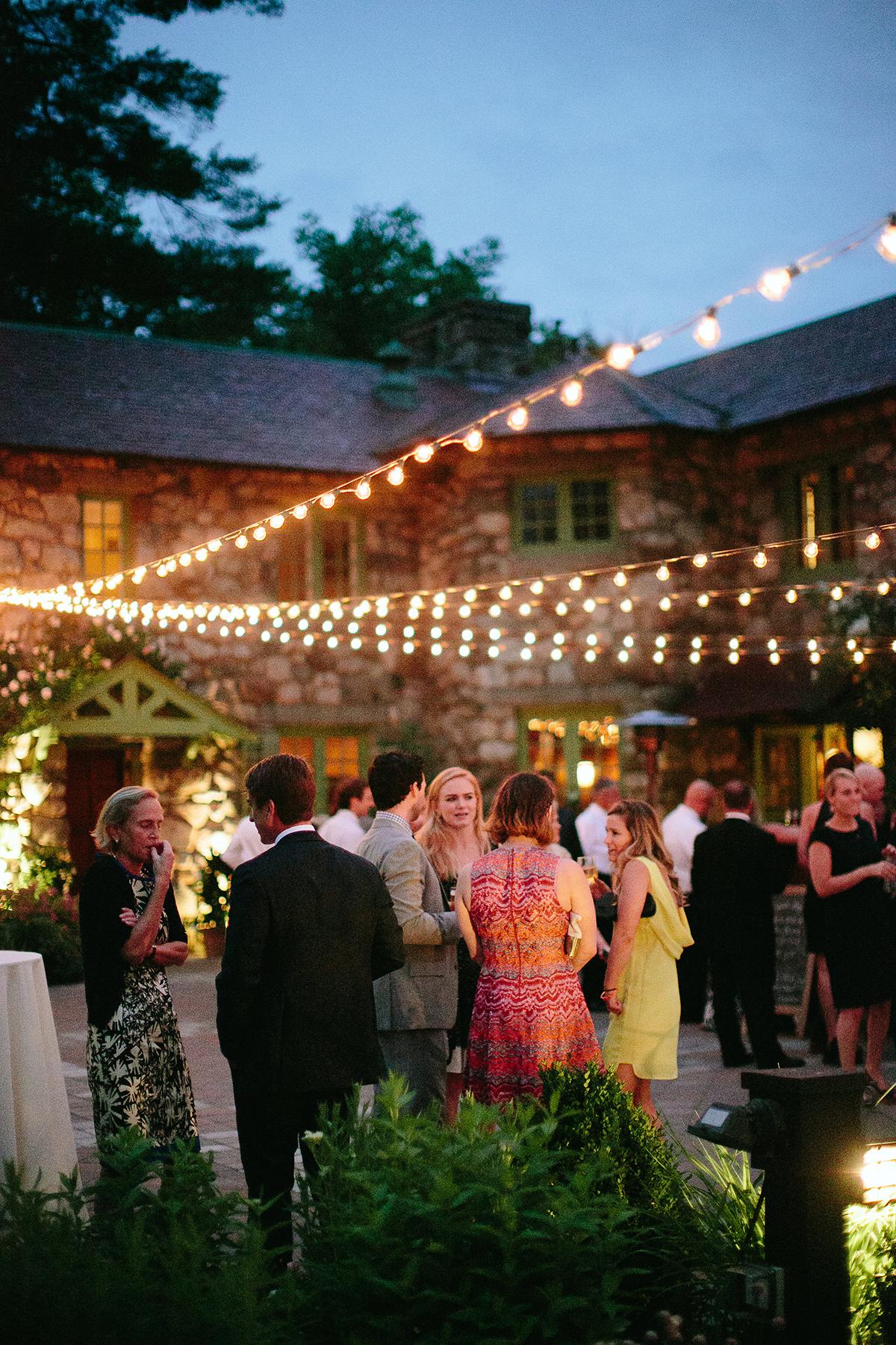 Outdoor evening event with people mingling under string lights.