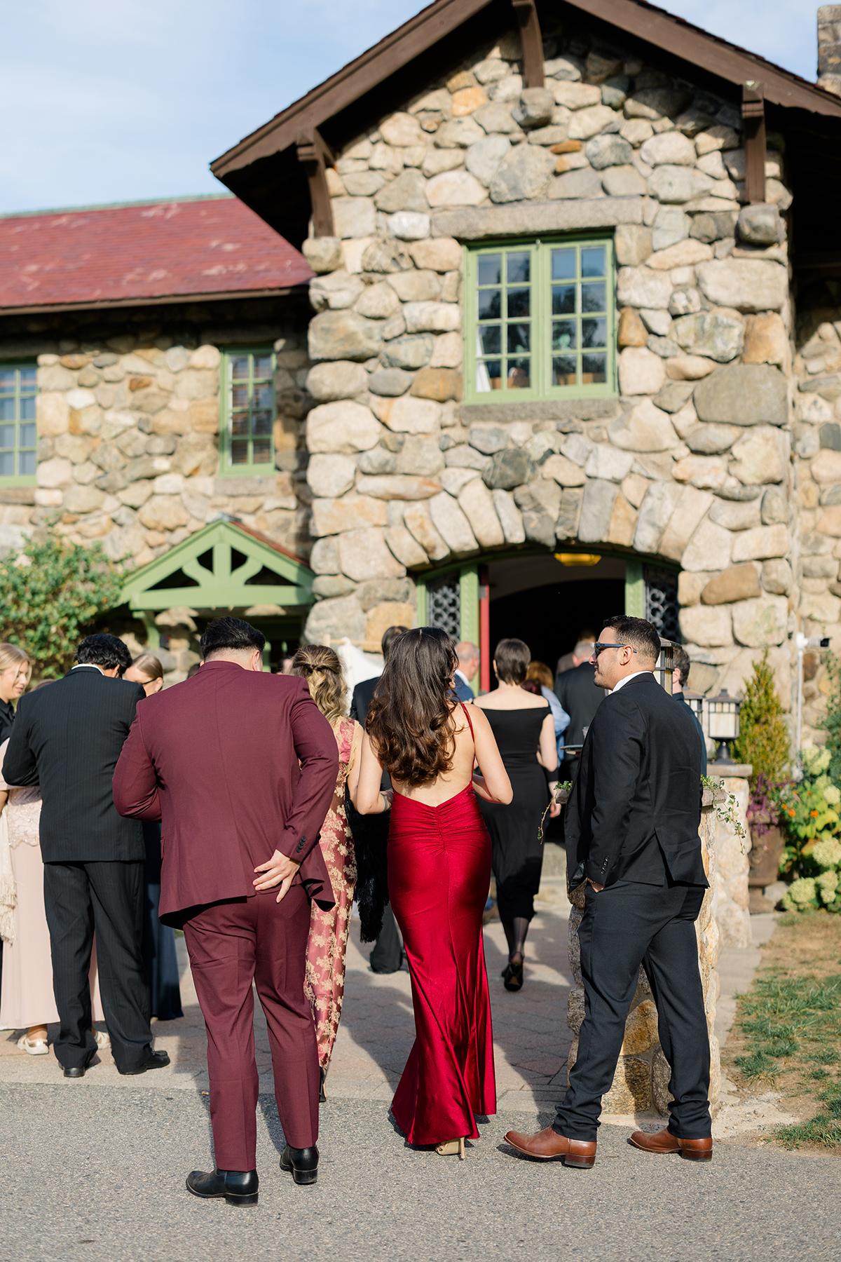 Guests in formal attire gather outside a stone building.