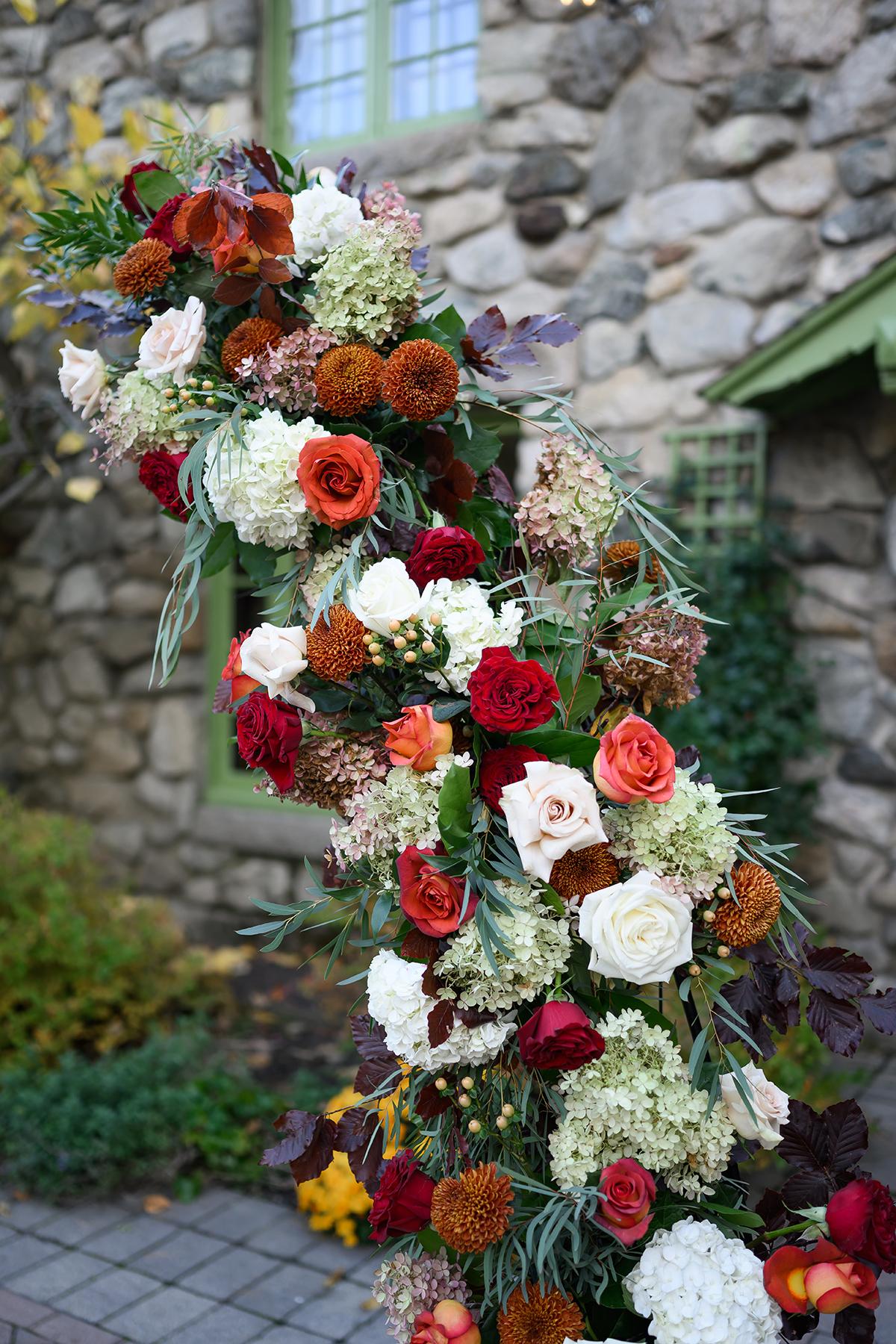 Floral arch with roses and hydrangeas in autumn colors, stone building background.