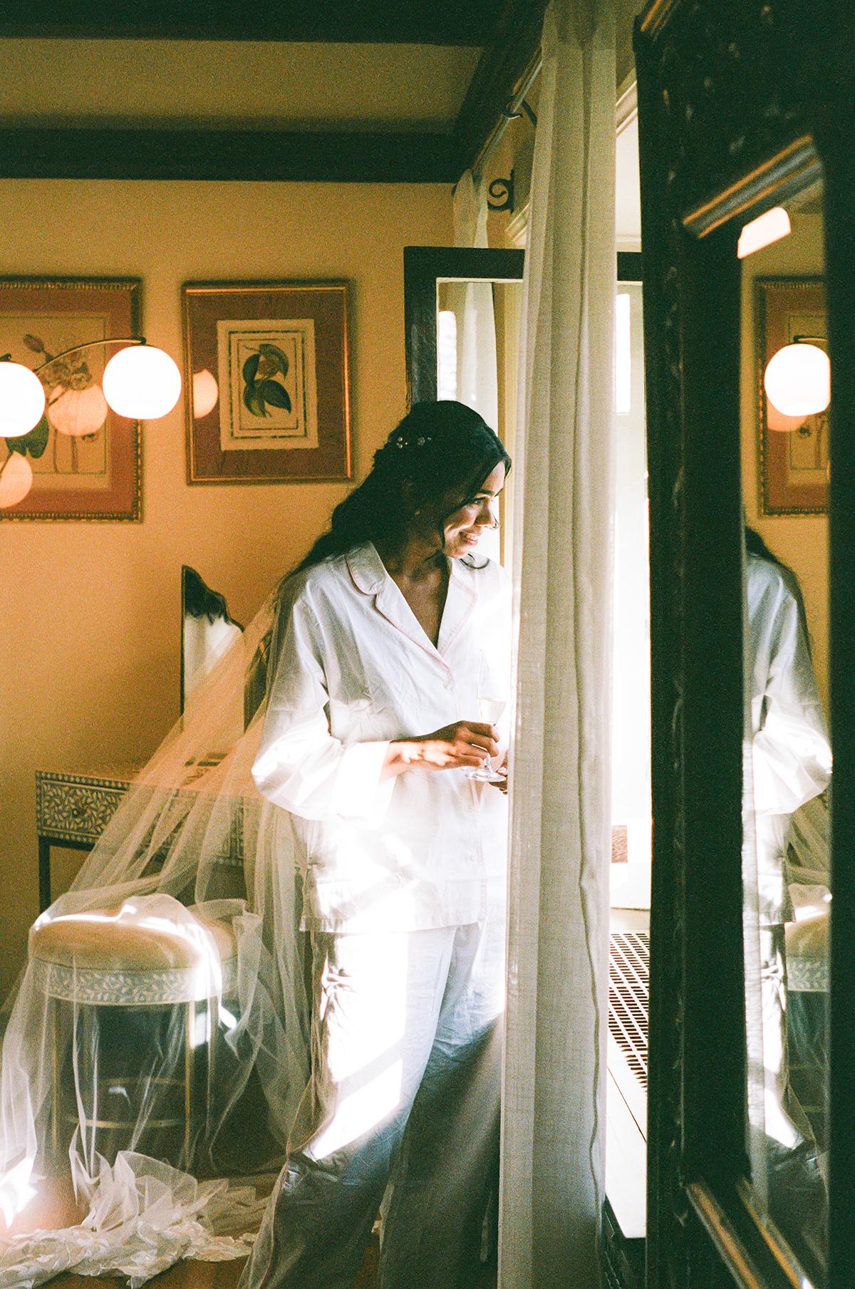 Woman in white robe standing by a window in a softly lit room.