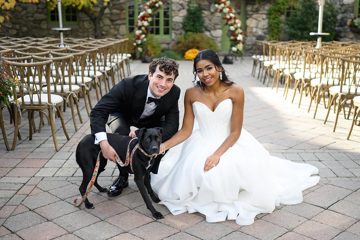 Wedding couple smiling with a dog in an outdoor ceremony setting.