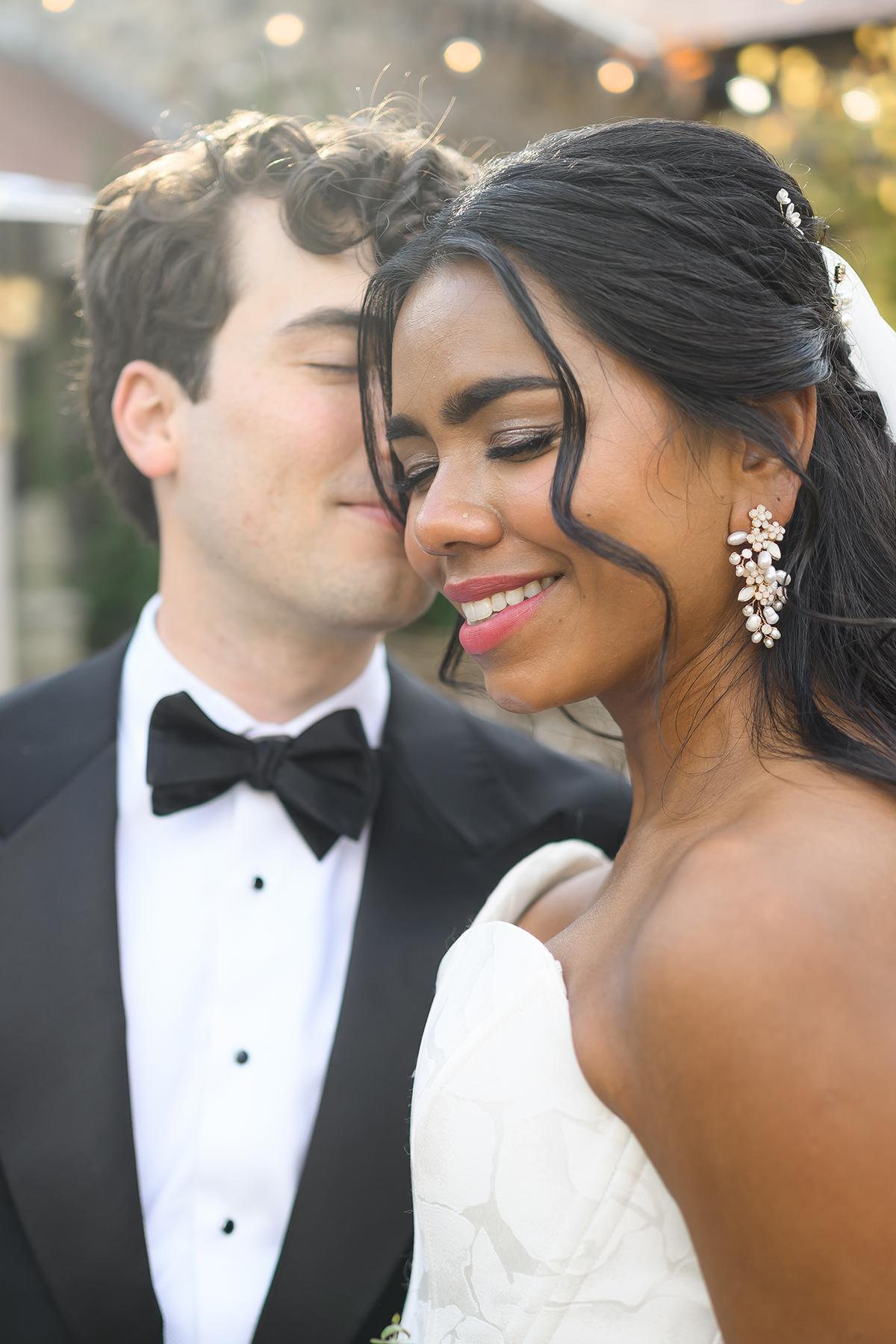 Bride smiling with groom in tuxedo at a wedding.