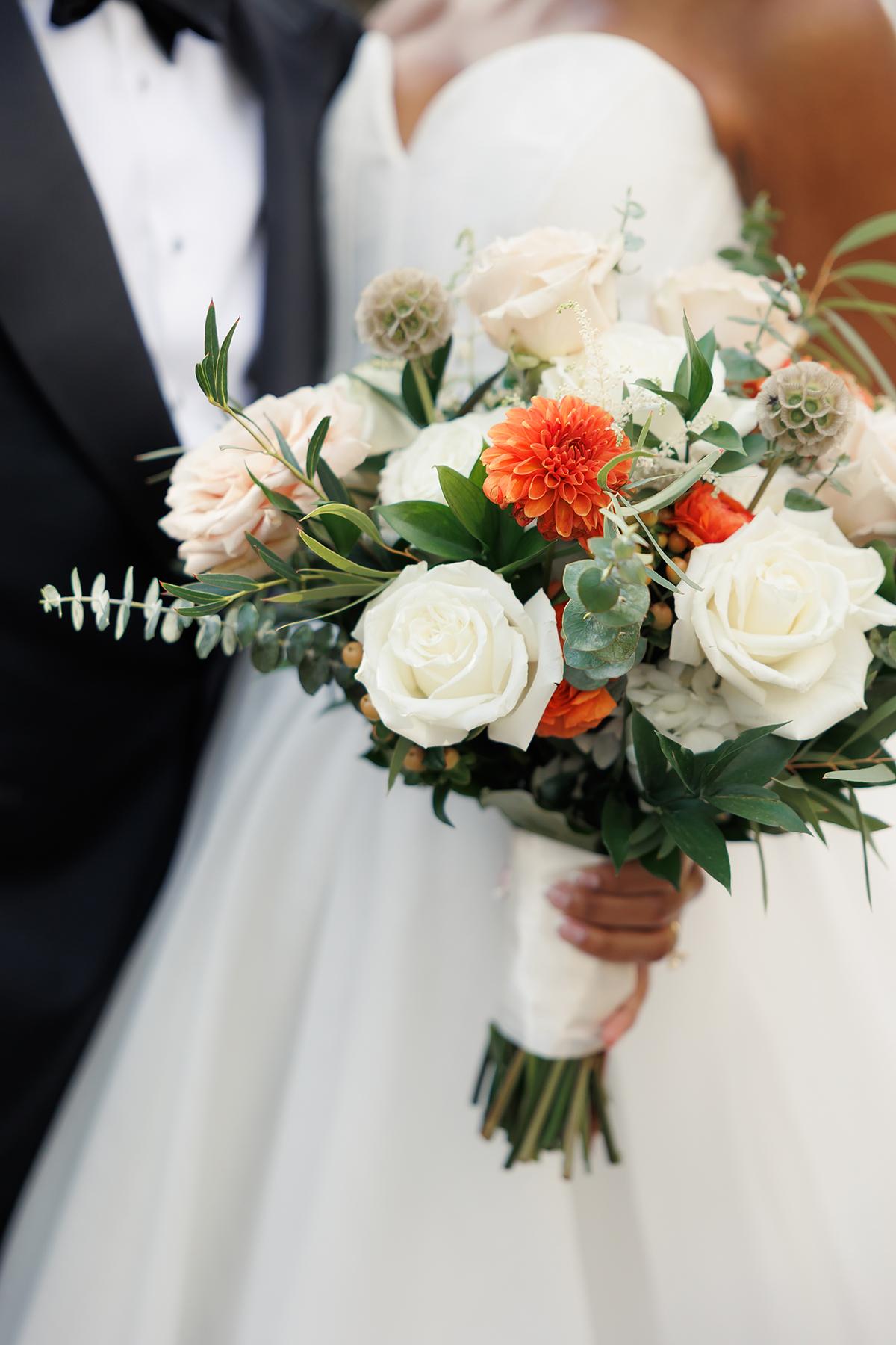 Bride holds bouquet of white and orange flowers in wedding dress.