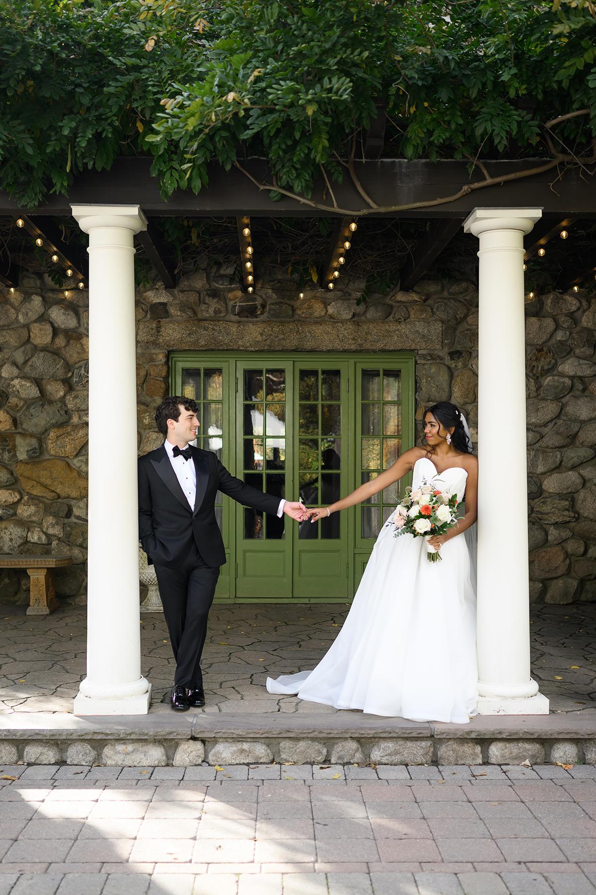 Bride and groom hold hands under a greenery-covered pergola.