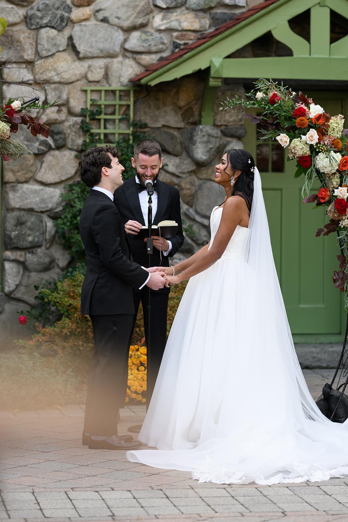 Wedding ceremony with couple holding hands, smiling, officiant reading.