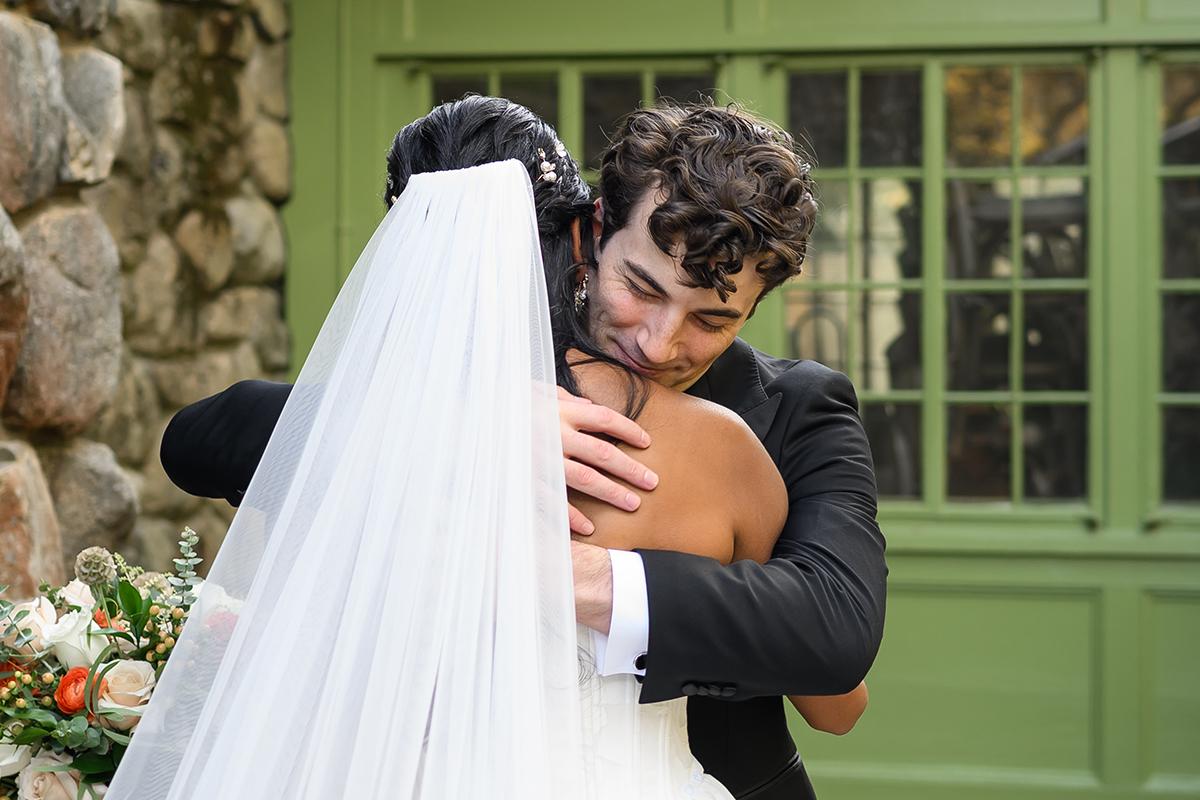 Groom and bride embracing warmly near stone wall.