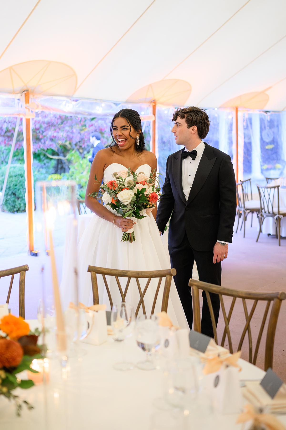 Bride and groom smile while holding hands at a decorated wedding reception.