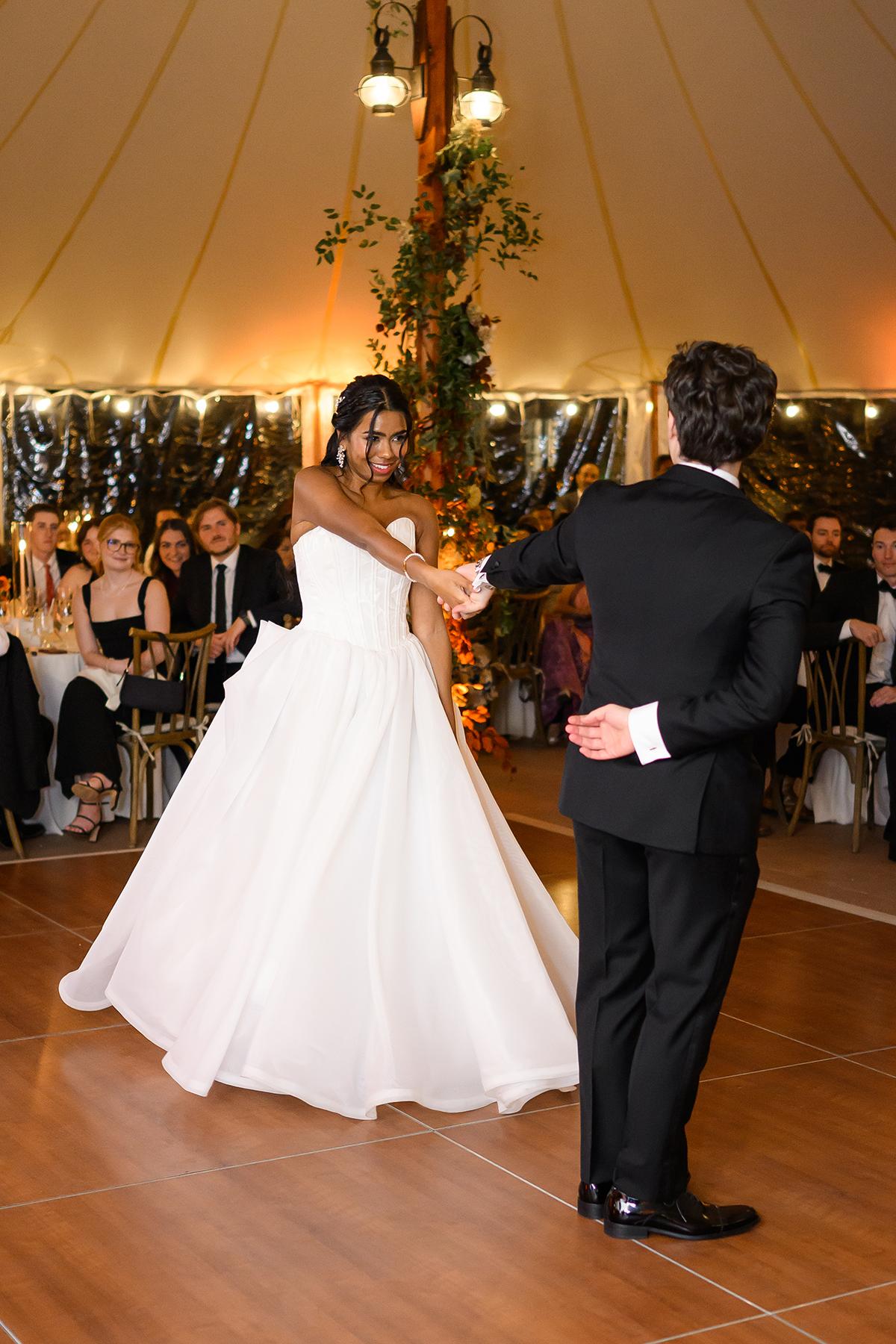 A couple dances in formal attire inside a warmly lit tent.