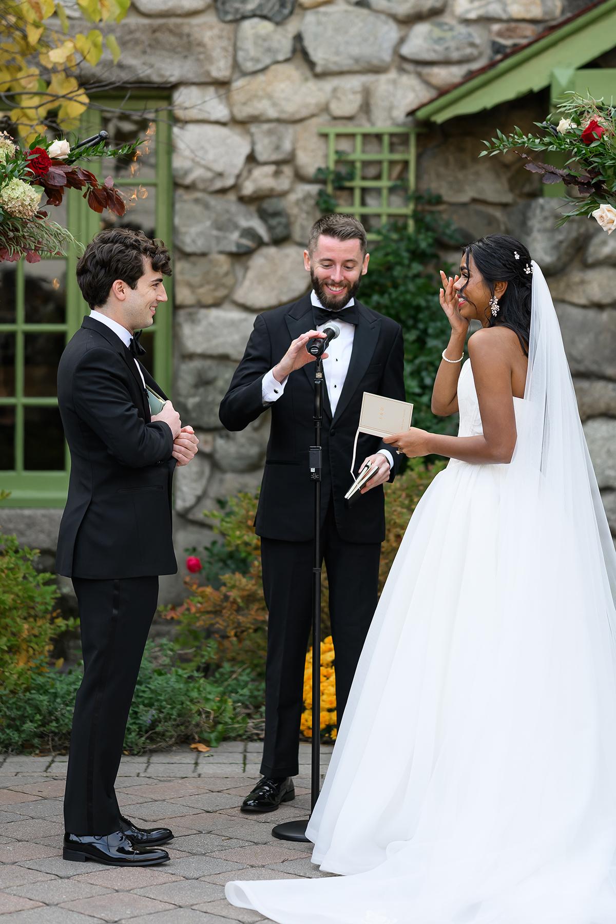 Bride and groom smiling during outdoor wedding ceremony with officiant.
