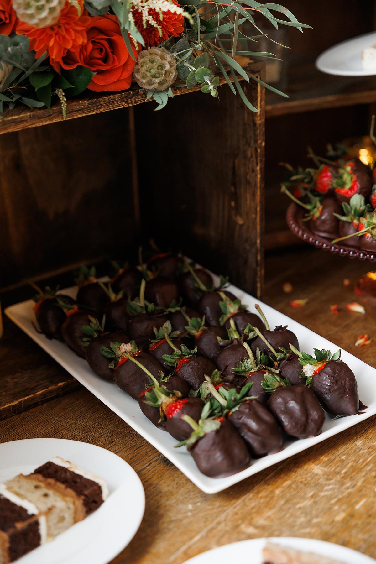 Chocolate-covered strawberries on a white platter, with orange flowers above.