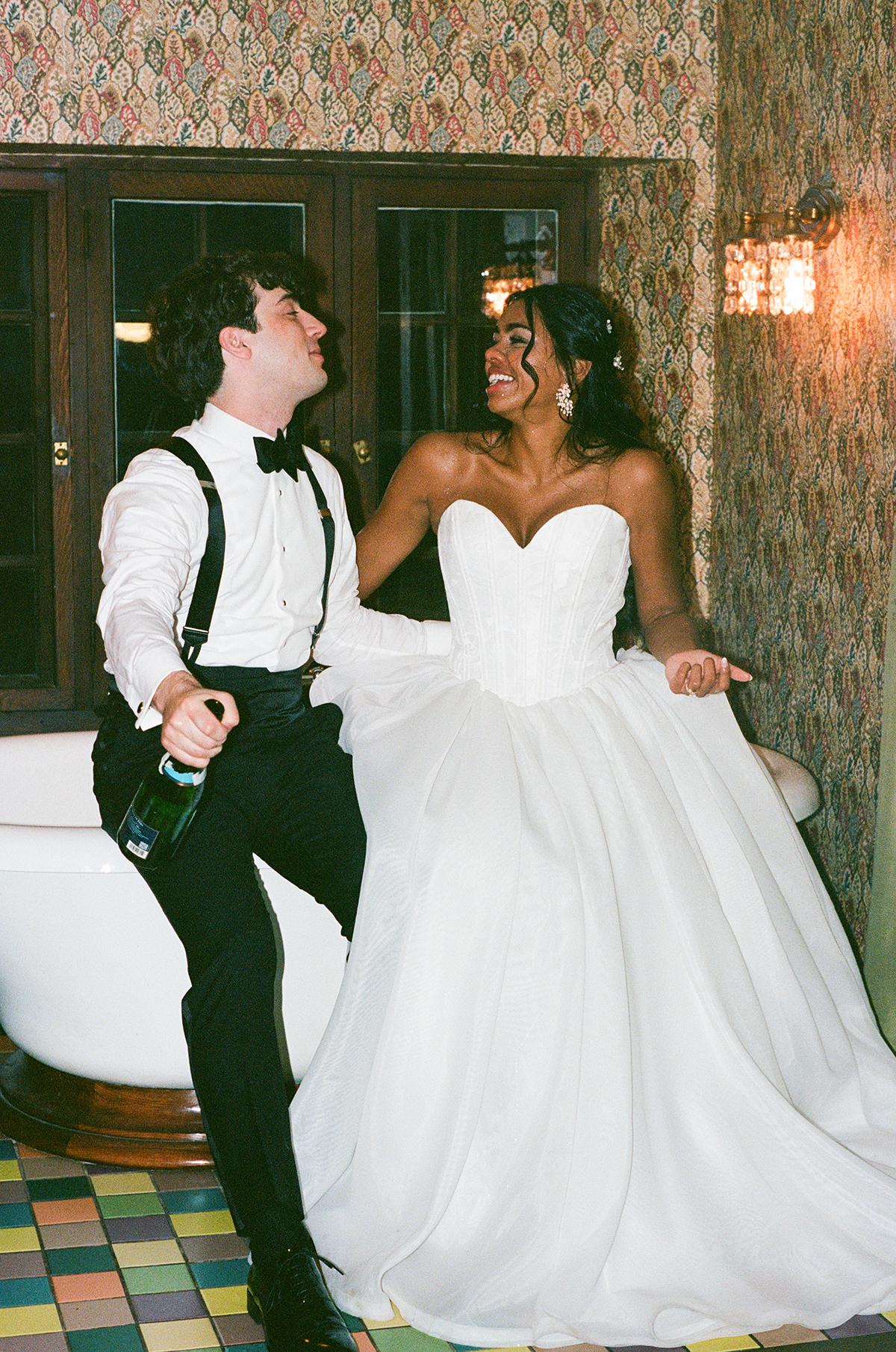 Bride and groom laughing, seated indoors in formal attire.