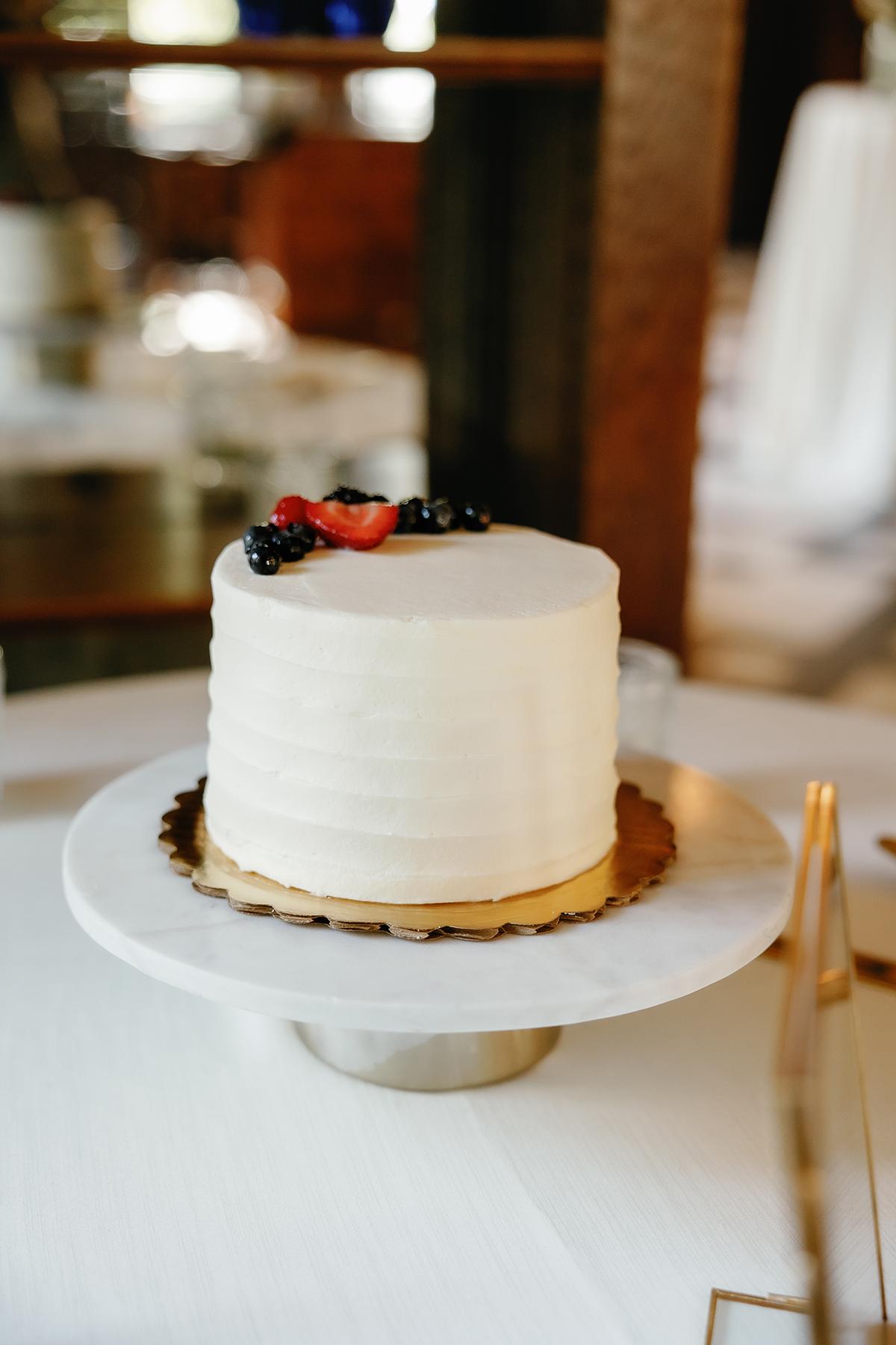 White frosted cake with berries on top, on a marble stand.
