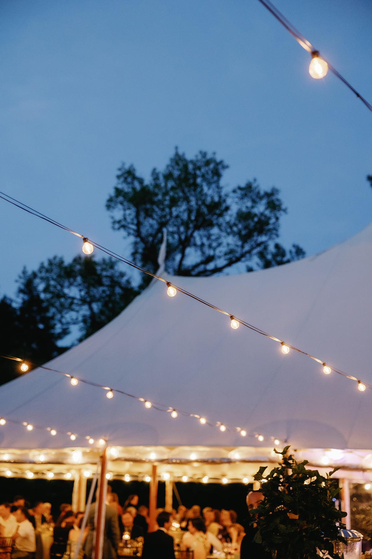 Outdoor wedding reception under a tent with string lights at dusk.